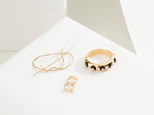 Gold jewelry pieces including a bangle bracelet with black studs, a twisted wire bracelet, and a stacked ring displayed on white surface.