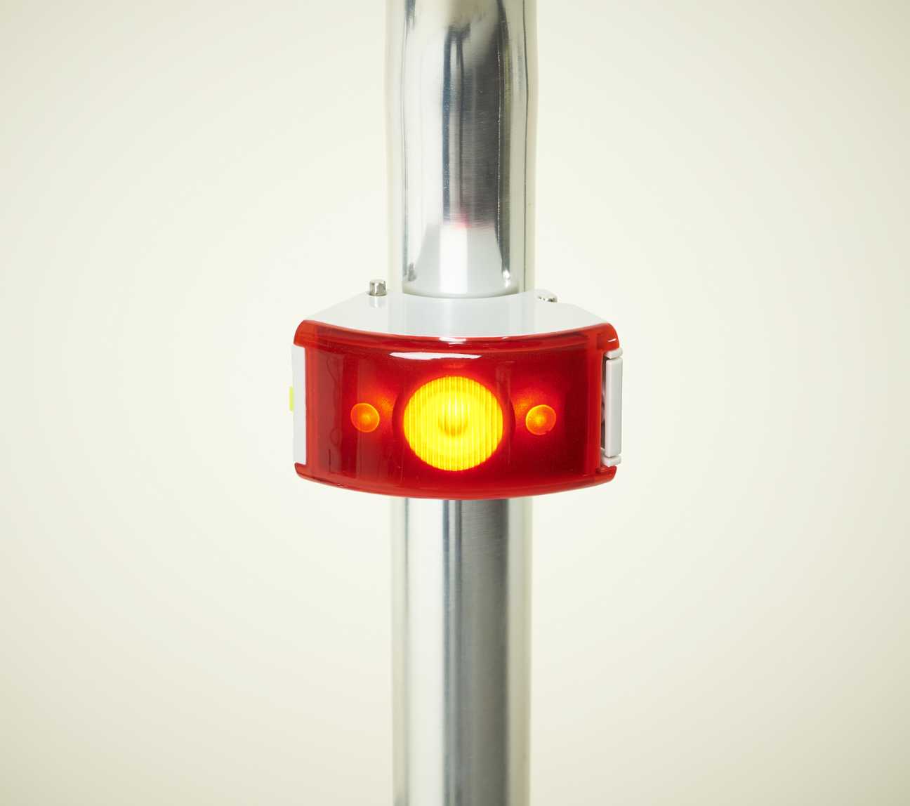 Bookman rechargeable bicycle rear light with red casing and yellow LED illuminated on metal seat post.
