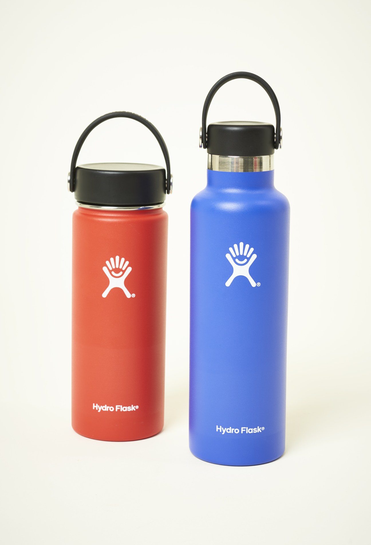 Two HydroFlask water bottles in red and blue with black lids and carrying handles.