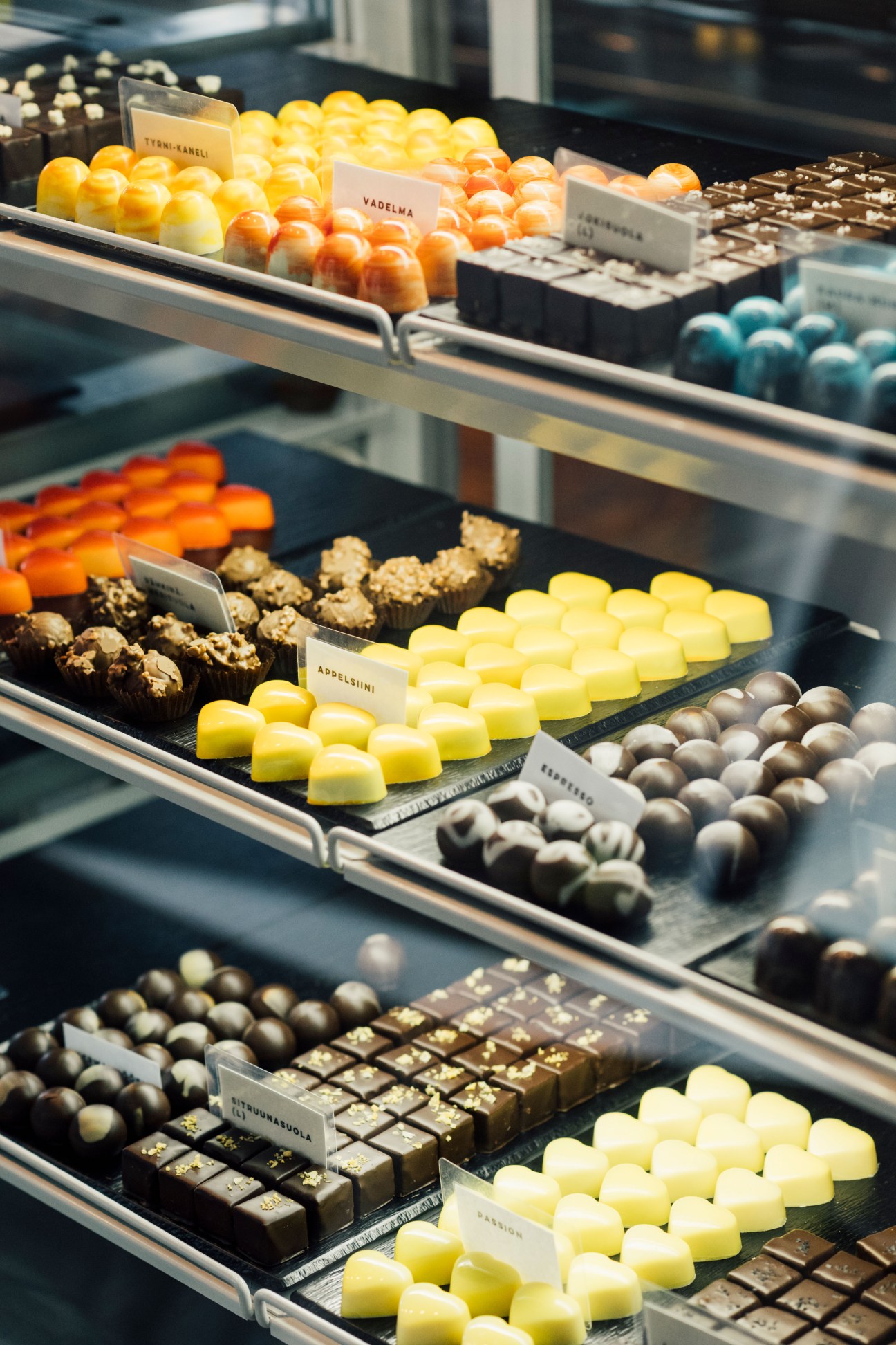 Display case of colorful artisanal chocolates and pralines with flavor labels at Chjoko chocolate shop in Helsinki.