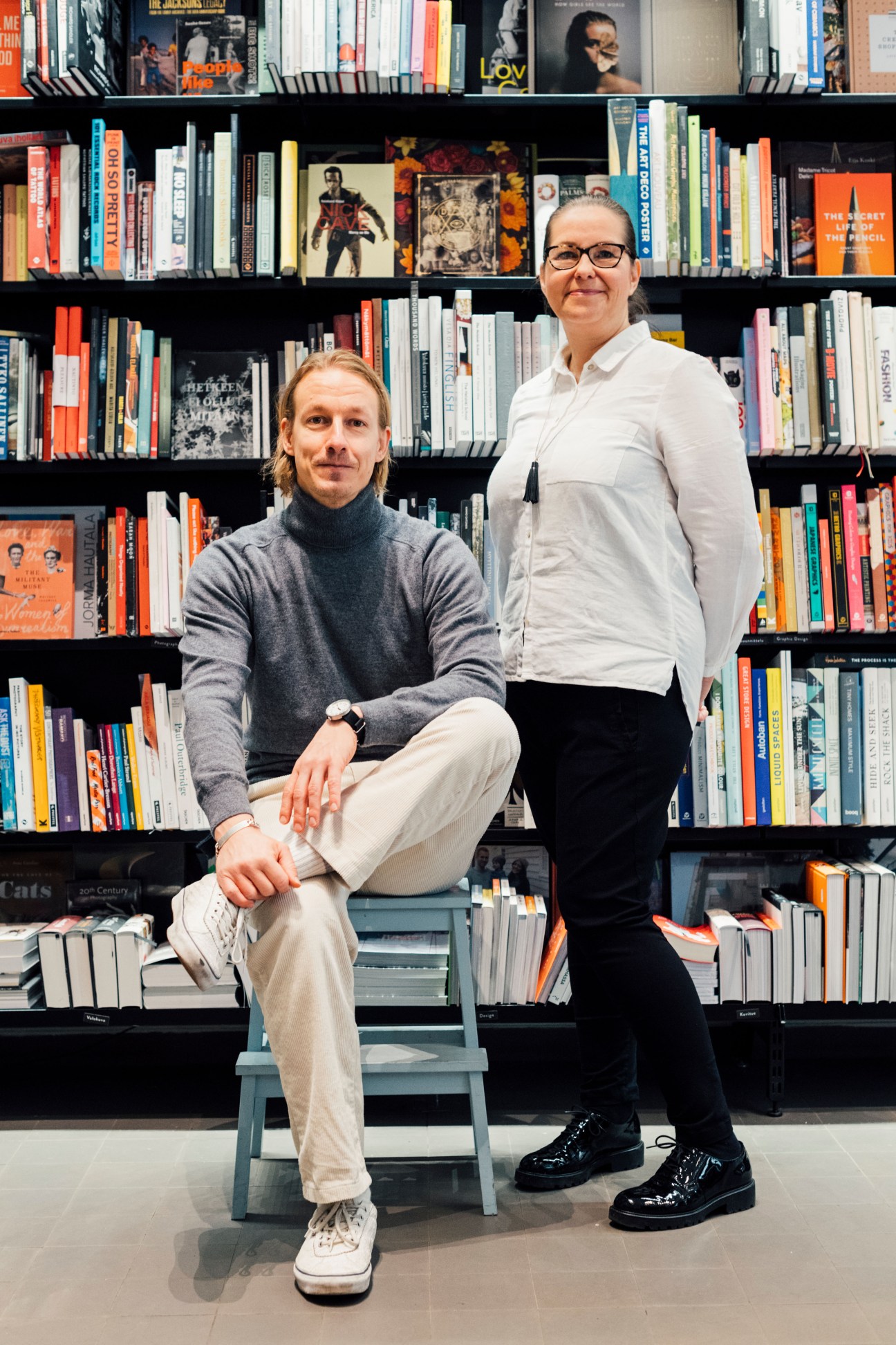Two people pose in front of bookshelves at Nide bookshop in Helsinki.