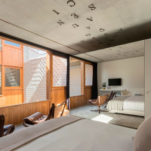 Modern hotel bedroom with exposed concrete ceiling, large windows, wooden paneling, and twin beds