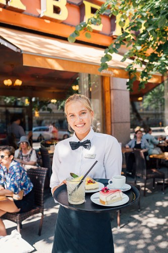Server at Ekberg café holding a tray with coffee and pastries in Helsinki.