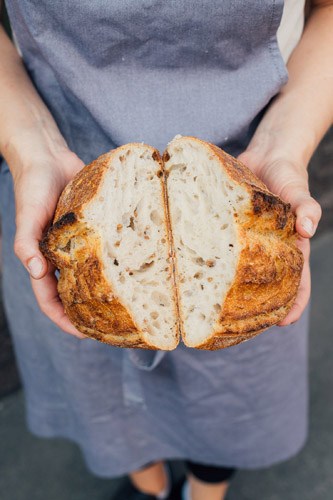 Hands holding a halved sourdough loaf from Levain bakery in Helsinki.