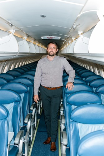 Thomas Hugo Møller standing in the aisle of an Embraer 195 aircraft with blue seats.