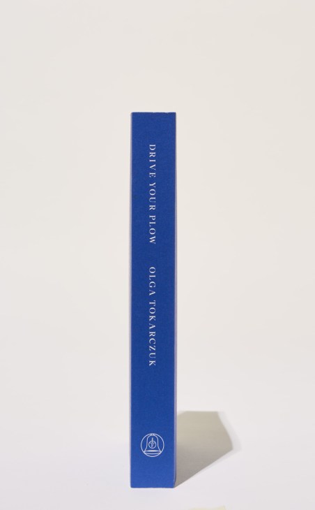 Blue hardcover book spine reading 'Drive Your Plow Over the Bones of the Dead' by Olga Tokarczuk with publisher logo.