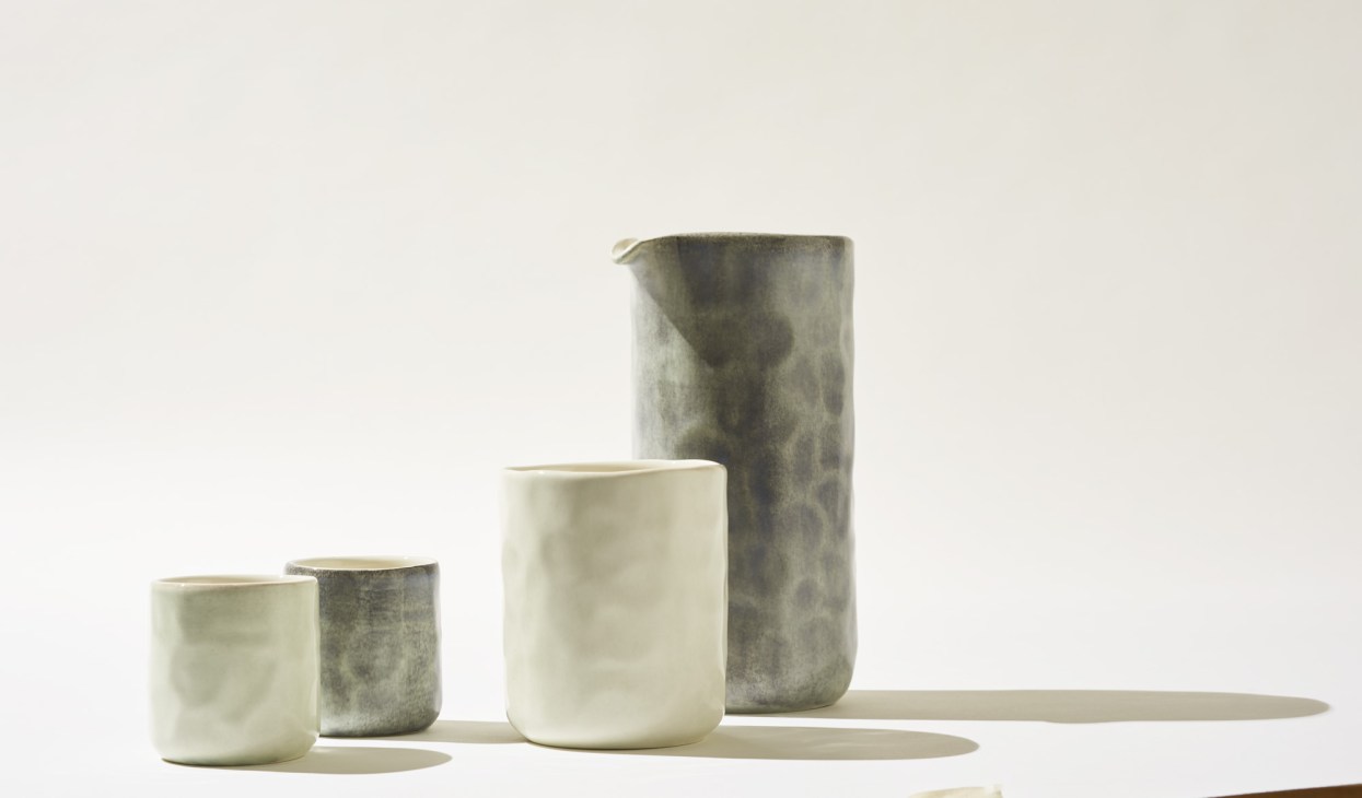 Collection of ceramic tableware by Mateus featuring unglazed vessels in neutral tones and hand-painted accents.