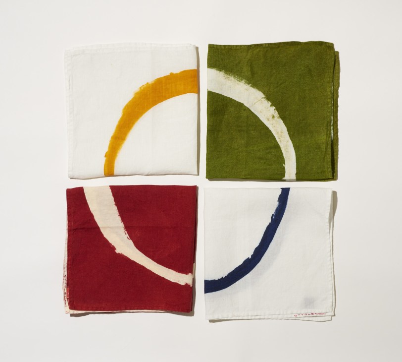 Four folded linen napkins in yellow, green, red and navy with curved white stripe details.