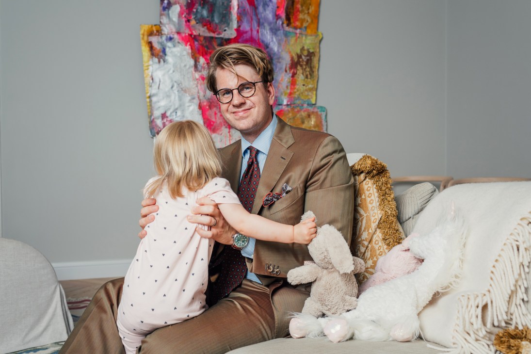 Niclas Ahlström, founder of Made by Choice, sits on a couch with a young child and stuffed toys, with colorful artwork on the wall behind.