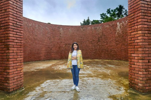 Person standing in an empty brick courtyard surrounded by tall red brick walls.