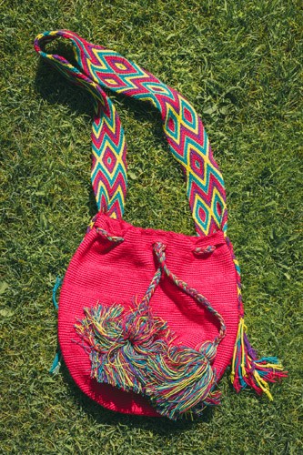 A pink woven pouch with colorful braided strap on green moss background