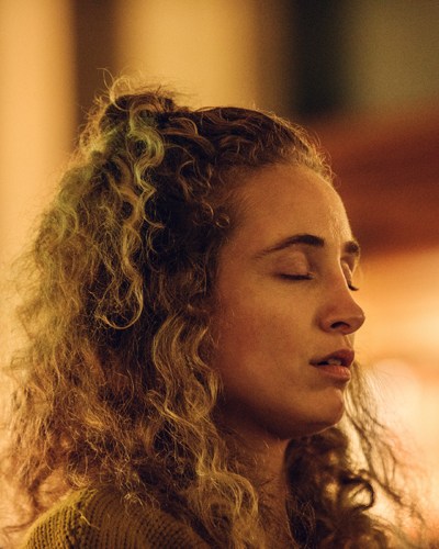 Woman with curly hair pulled back, eyes closed, in profile during a meditation session.