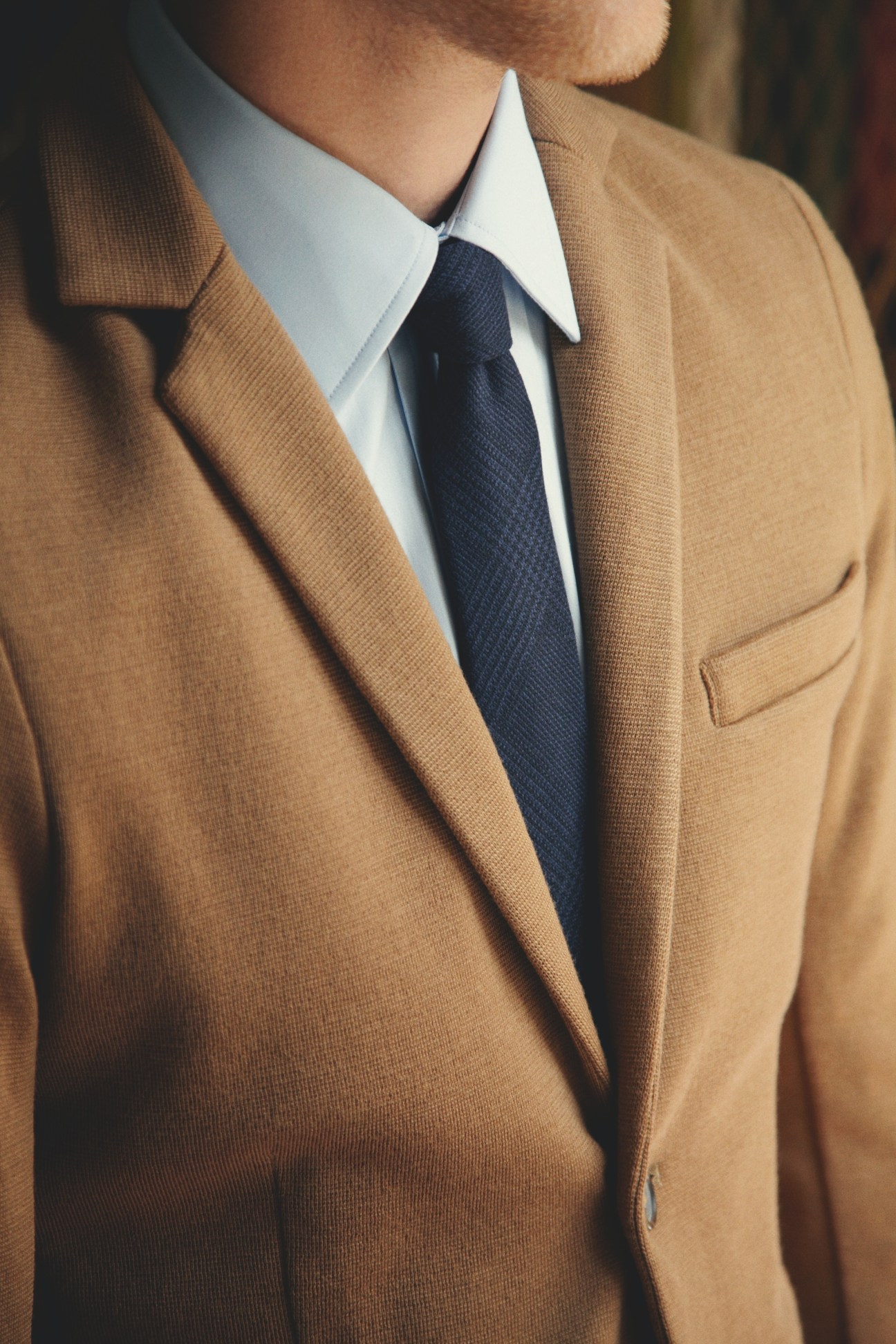 Close-up of a camel-colored blazer worn with a white dress shirt and navy tie.