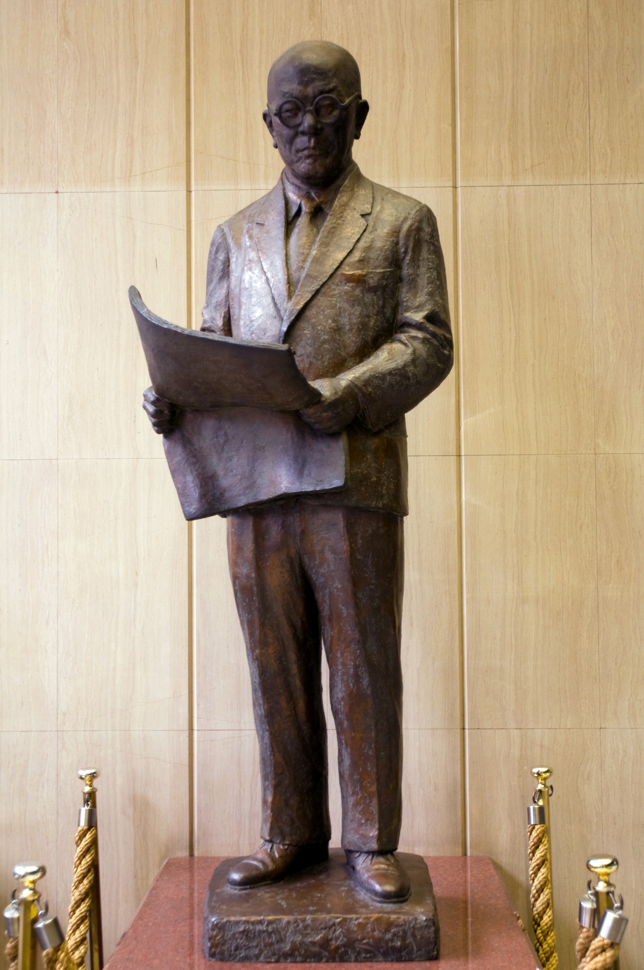Bronze statue of a man in glasses and business suit holding an open newspaper.