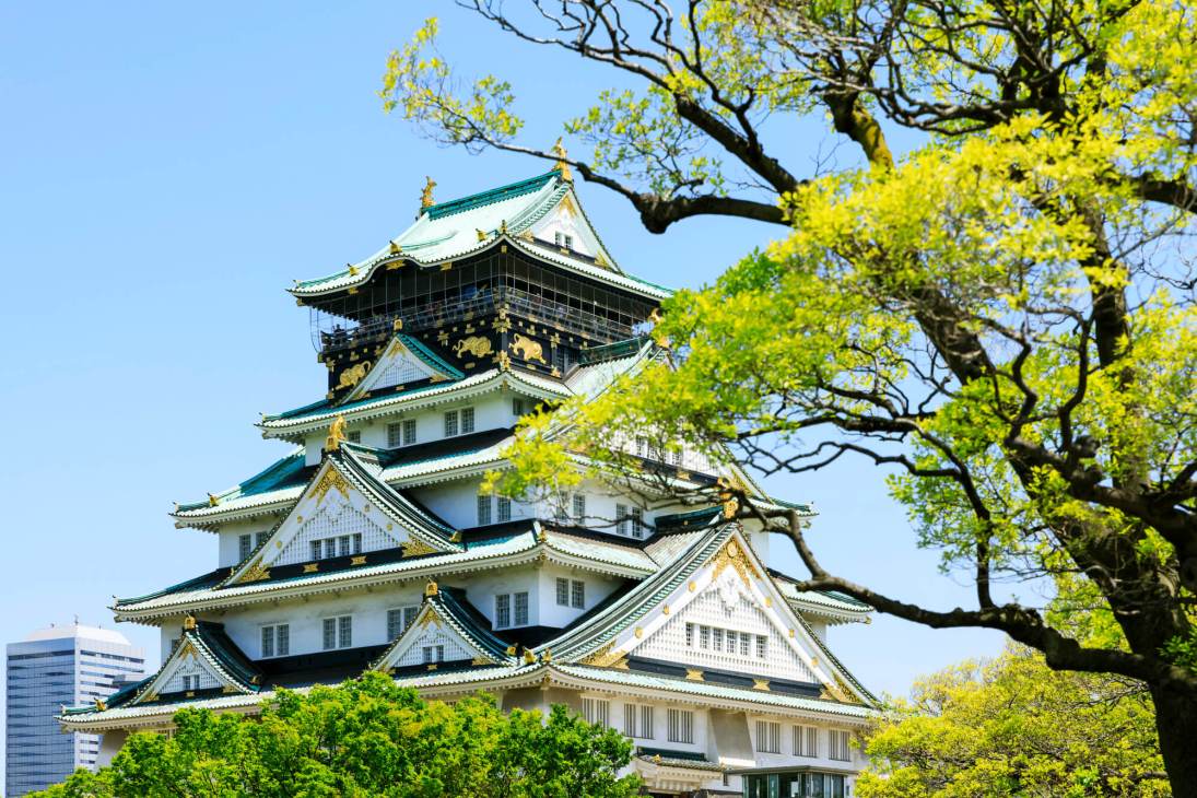 Osaka Castle with distinctive multi-tiered roofs and golden ornaments surrounded by green trees.