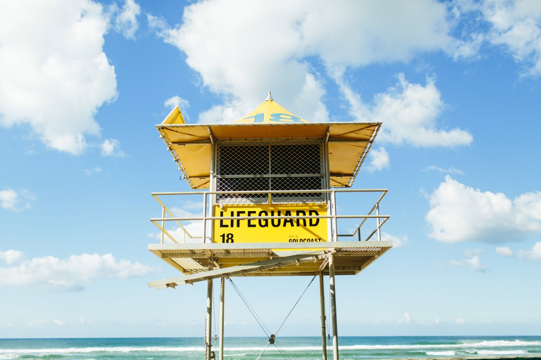 Yellow lifeguard tower numbered 18 on stilts against blue sky and ocean at Burleigh Heads Beach