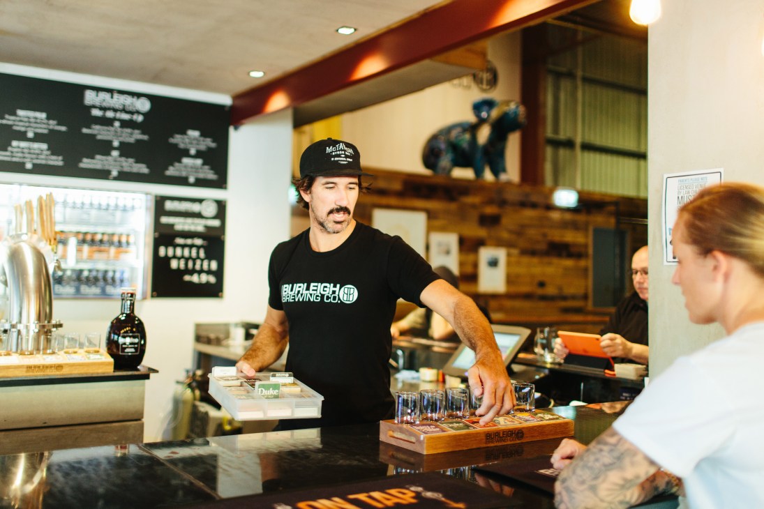 A bartender in a Burleigh Brewing Co t-shirt serves beer samples at the brewery bar