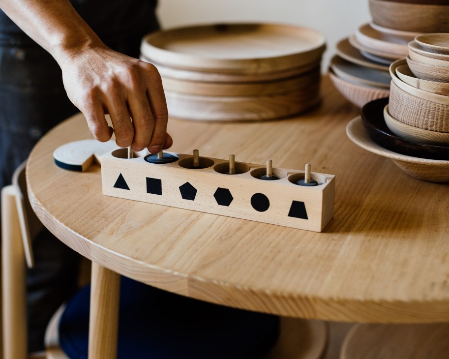 Hand placing a wooden spinning top with geometric shapes into a stand designed by A/I Studio.