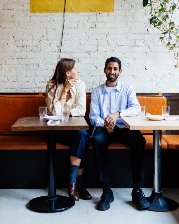 Two people seated on an orange leather booth against a white brick wall in a modern restaurant.