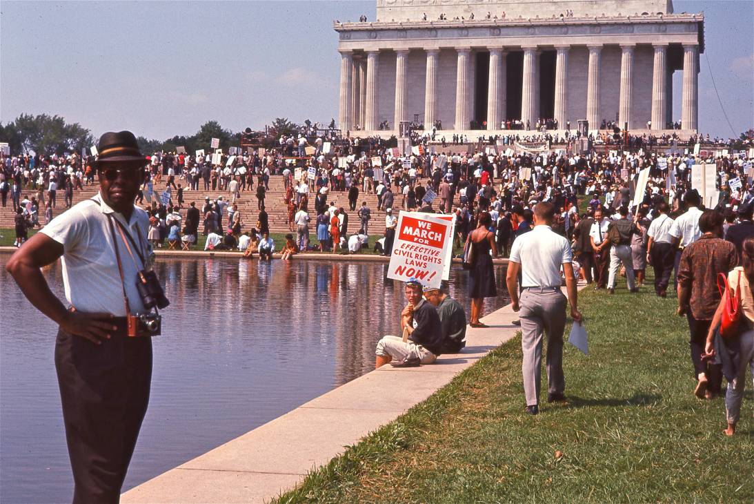 Civil rights march at the Lincoln Memorial with crowds holding protest signs and the iconic columned building in background.