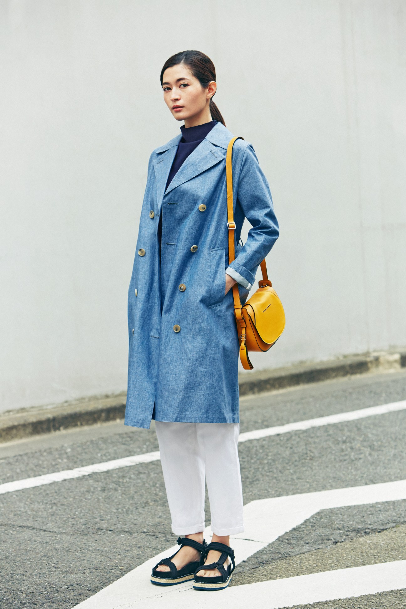 Woman wearing light blue denim coat, navy turtleneck, white pants, yellow shoulder bag and black platform sandals.