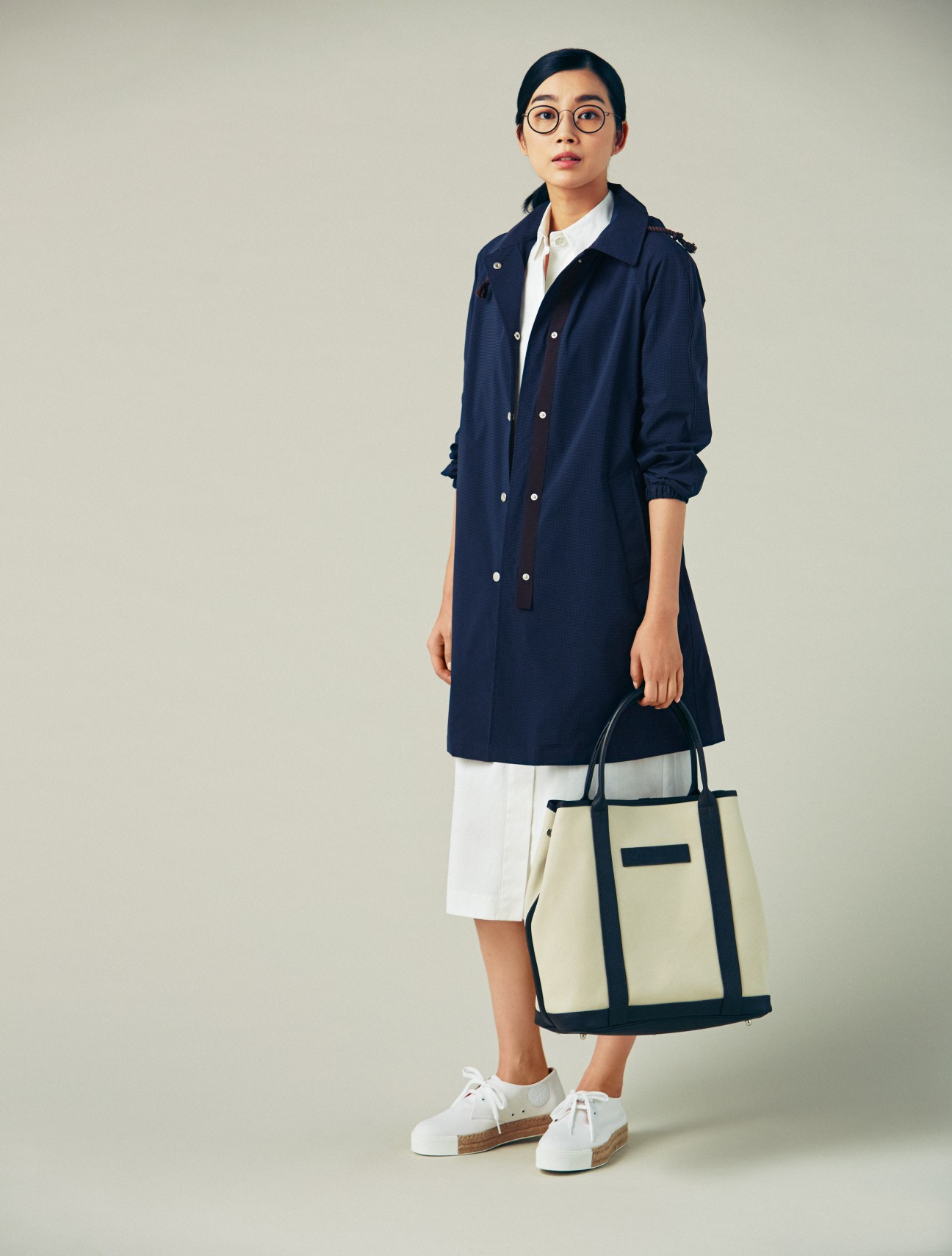 Woman wearing navy Sealup coat, white dress, white Hermès trainers, Lindberg glasses, and Felisi bag.