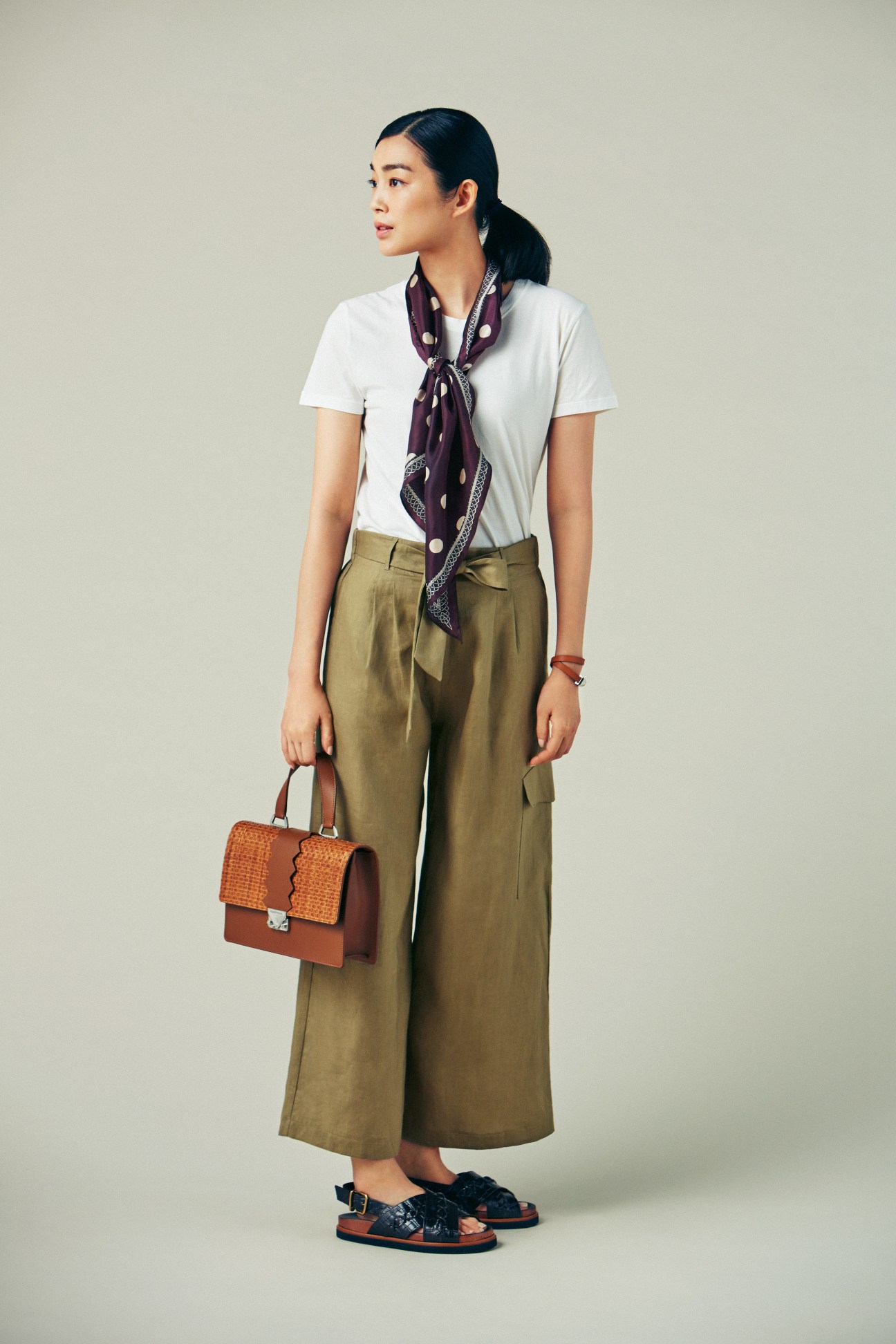 Woman wearing Gucci jacket and shirt with Acne Studios jeans and Lindberg glasses, holding brown woven leather handbag and wearing navy sandals.