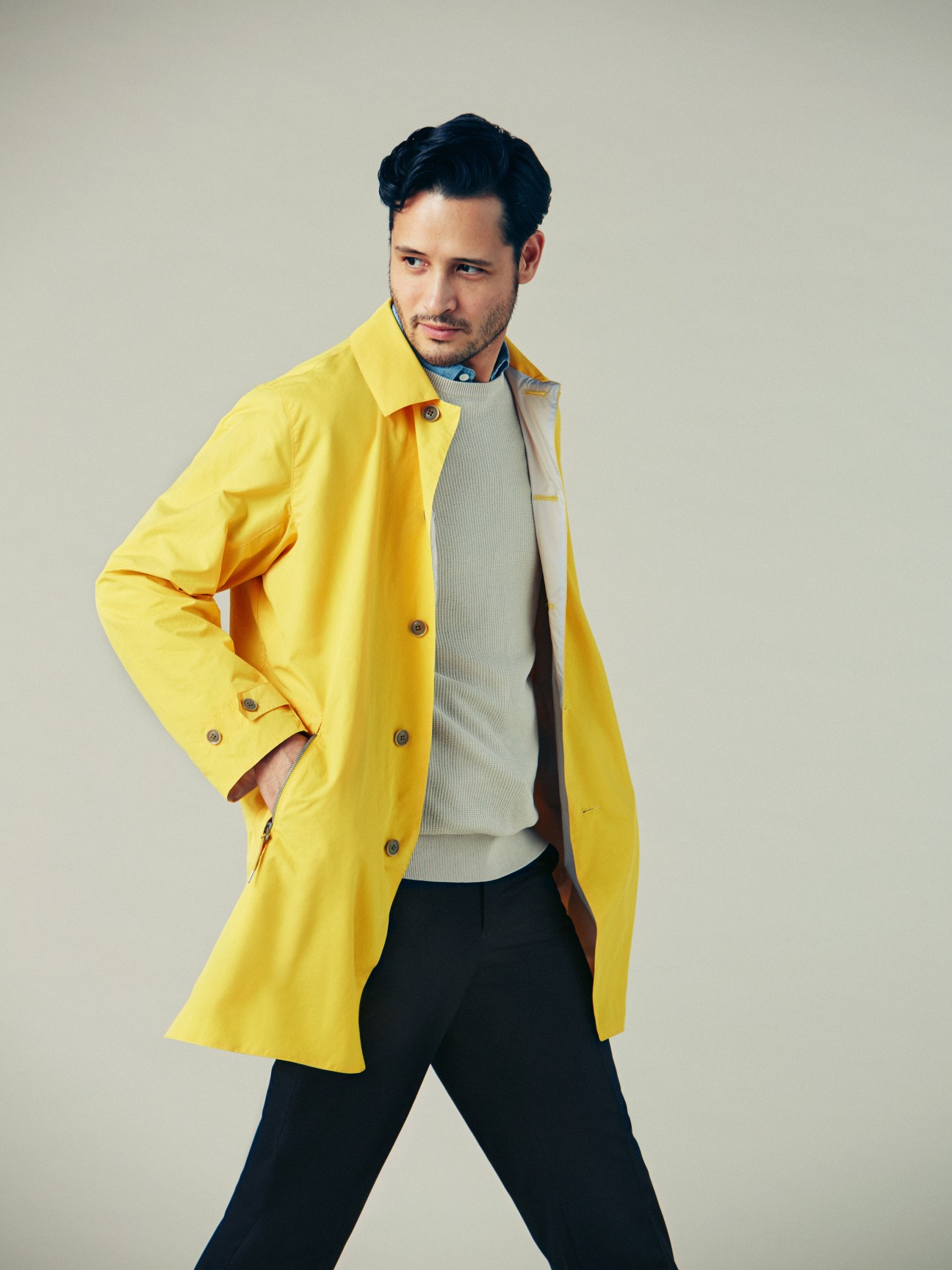 Man wearing a bright yellow coat over a cream sweater and dark trousers against a neutral background.