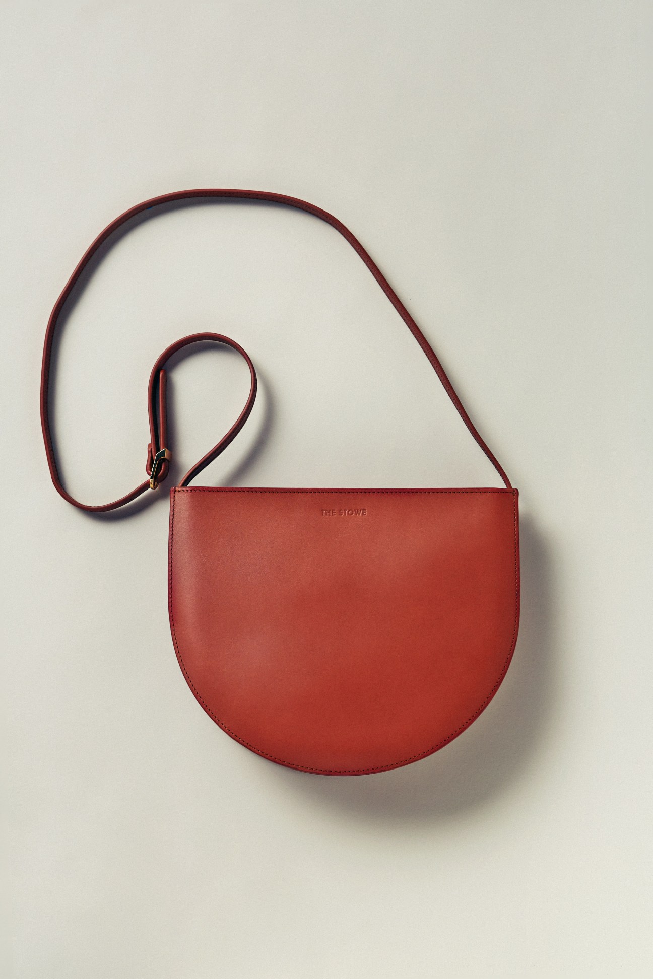 Red leather The Stowe shoulder bag with long strap displayed against white background.