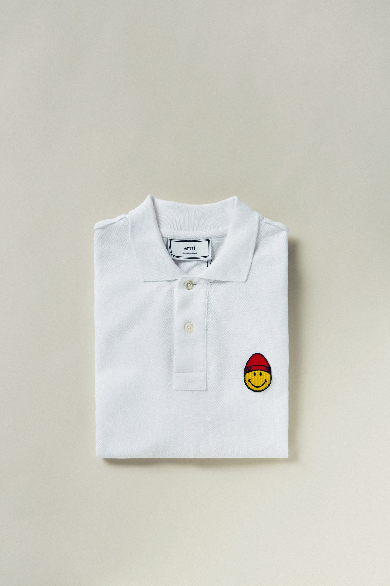 White polo shirt by Ami with embroidered smiley face wearing red beanie