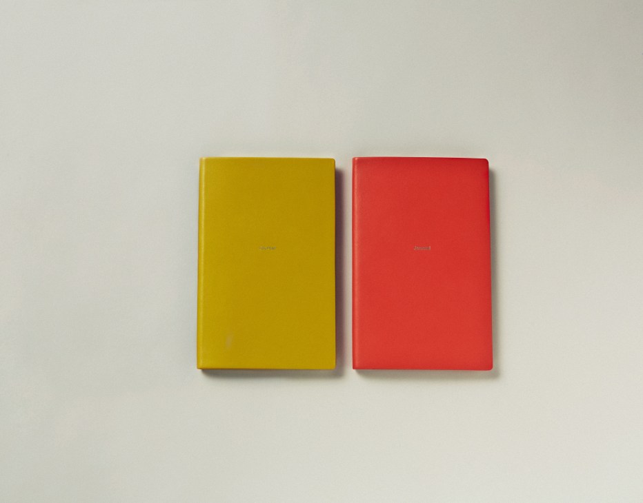 Two colored notebooks—one mustard yellow and one red—displayed side by side on a neutral background.