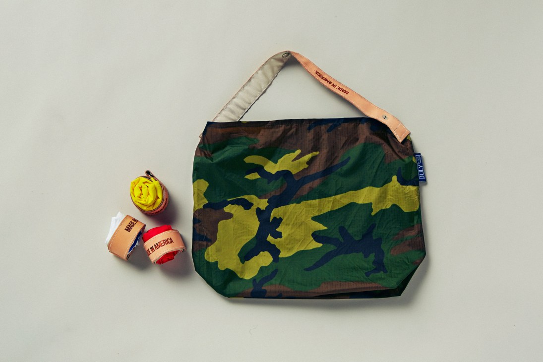 Camouflage patterned tote bag with tan leather handles and yellow accents displayed flat.