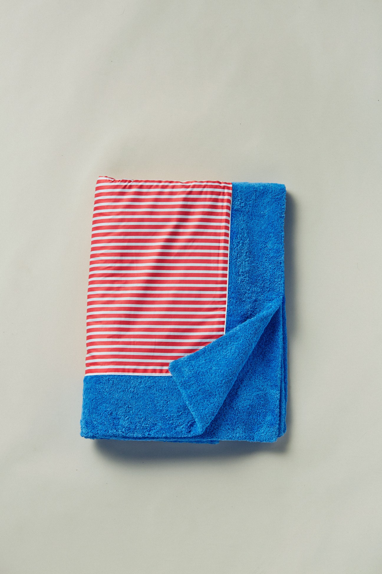 Red and white striped towel folded with blue terry cloth towel on neutral background.
