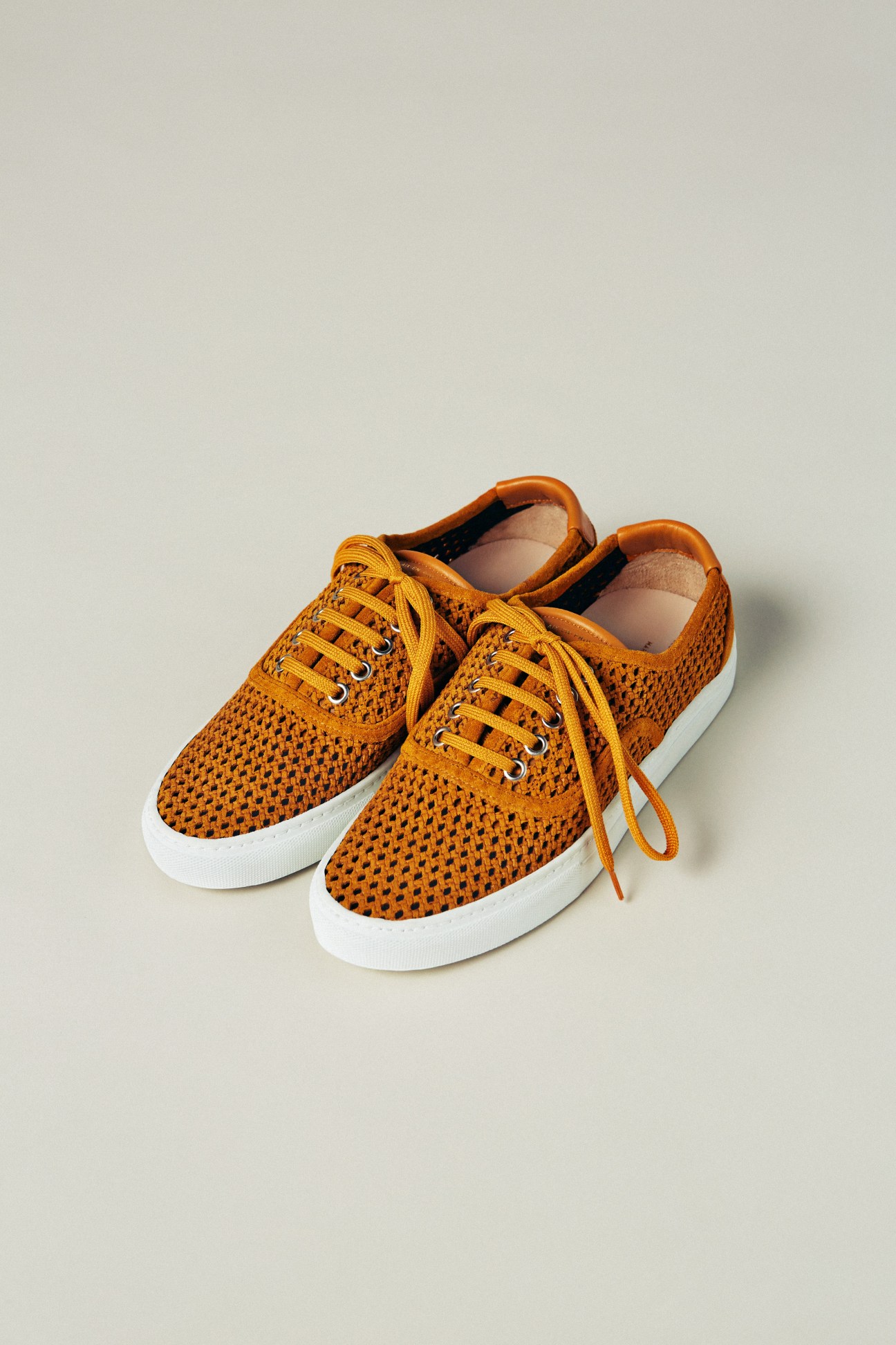 Orange perforated suede trainers with white sole and yellow laces.