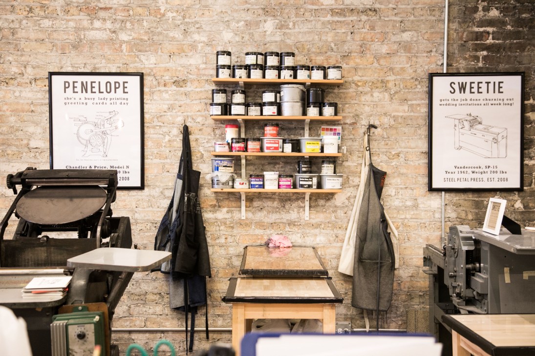 Steel Petal Press letterpress shop interior with wooden shelves displaying ink jars and printing supplies.