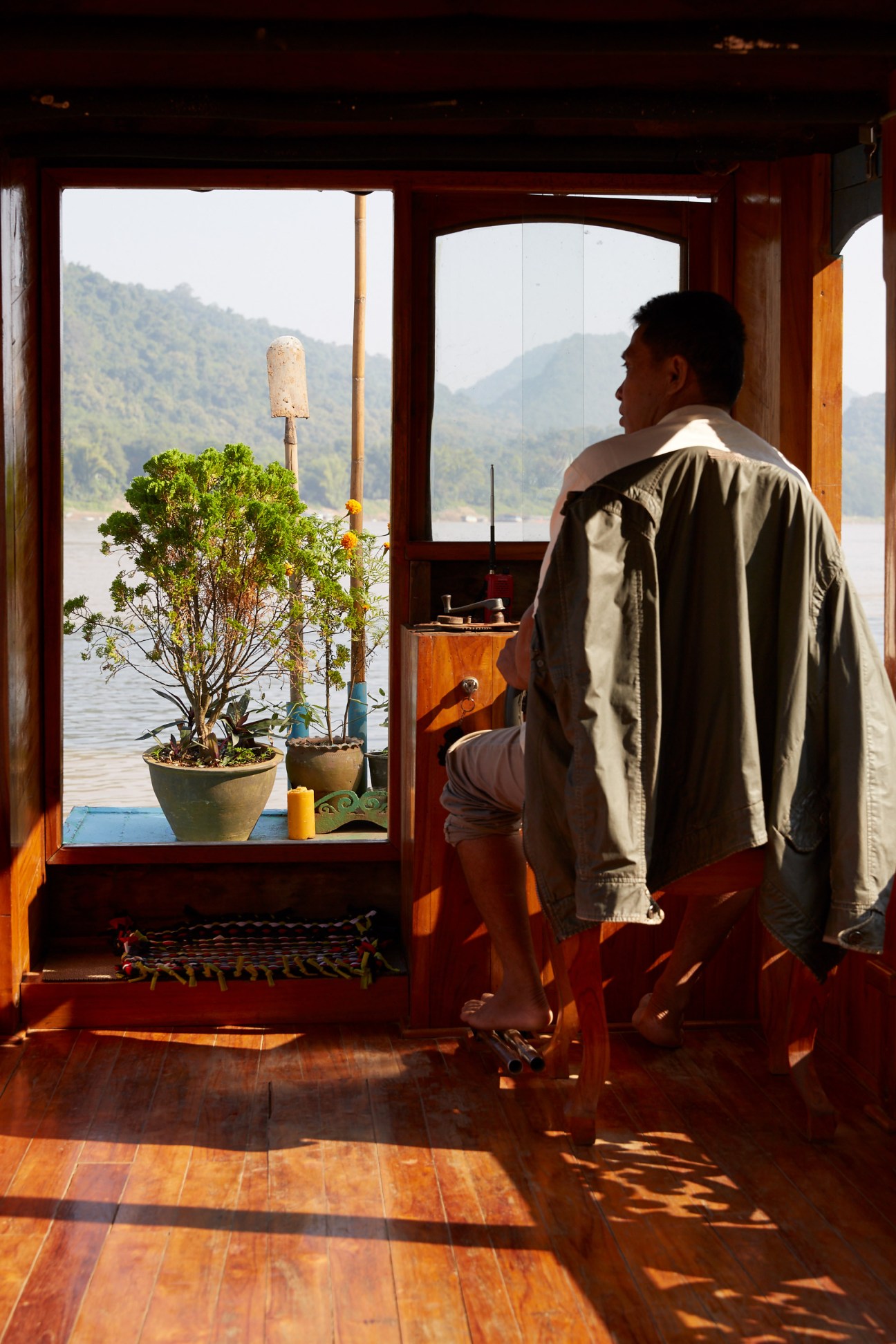 Man gazes out at Mekong River and forested mountains through open window of Belle Rive Boutique Hotel in Luang Prabang.