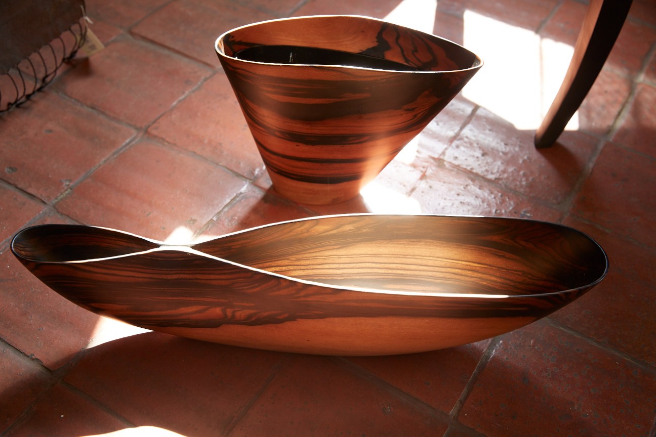Ebony wooden bowls and serving pieces with striped grain patterns on terracotta tiles.