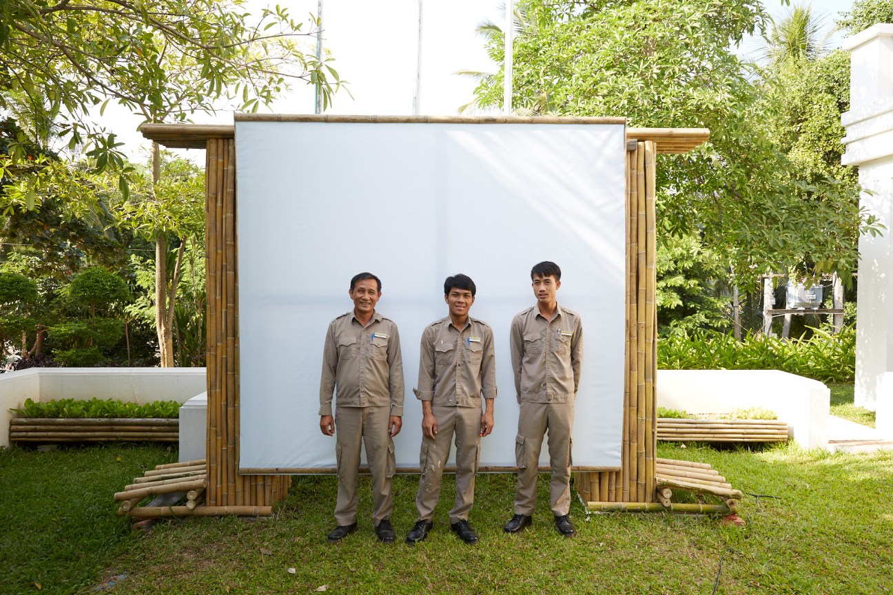Three staff members in khaki uniforms stand in front of a white panel at Pha Tad Ke Botanical Garden.