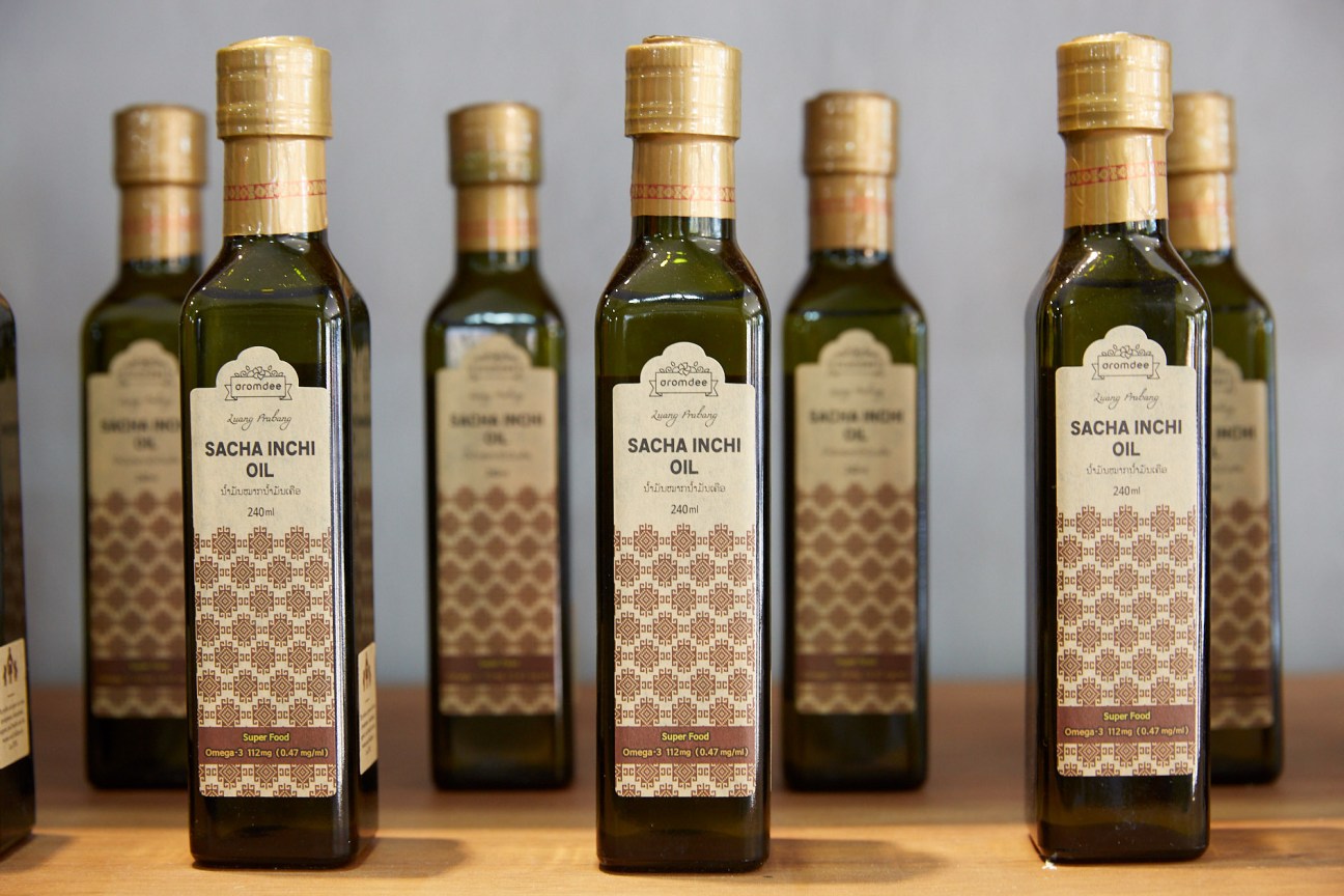 Bottles of Aromdee sacha inchi oil with gold caps and patterned labels on a wooden surface.