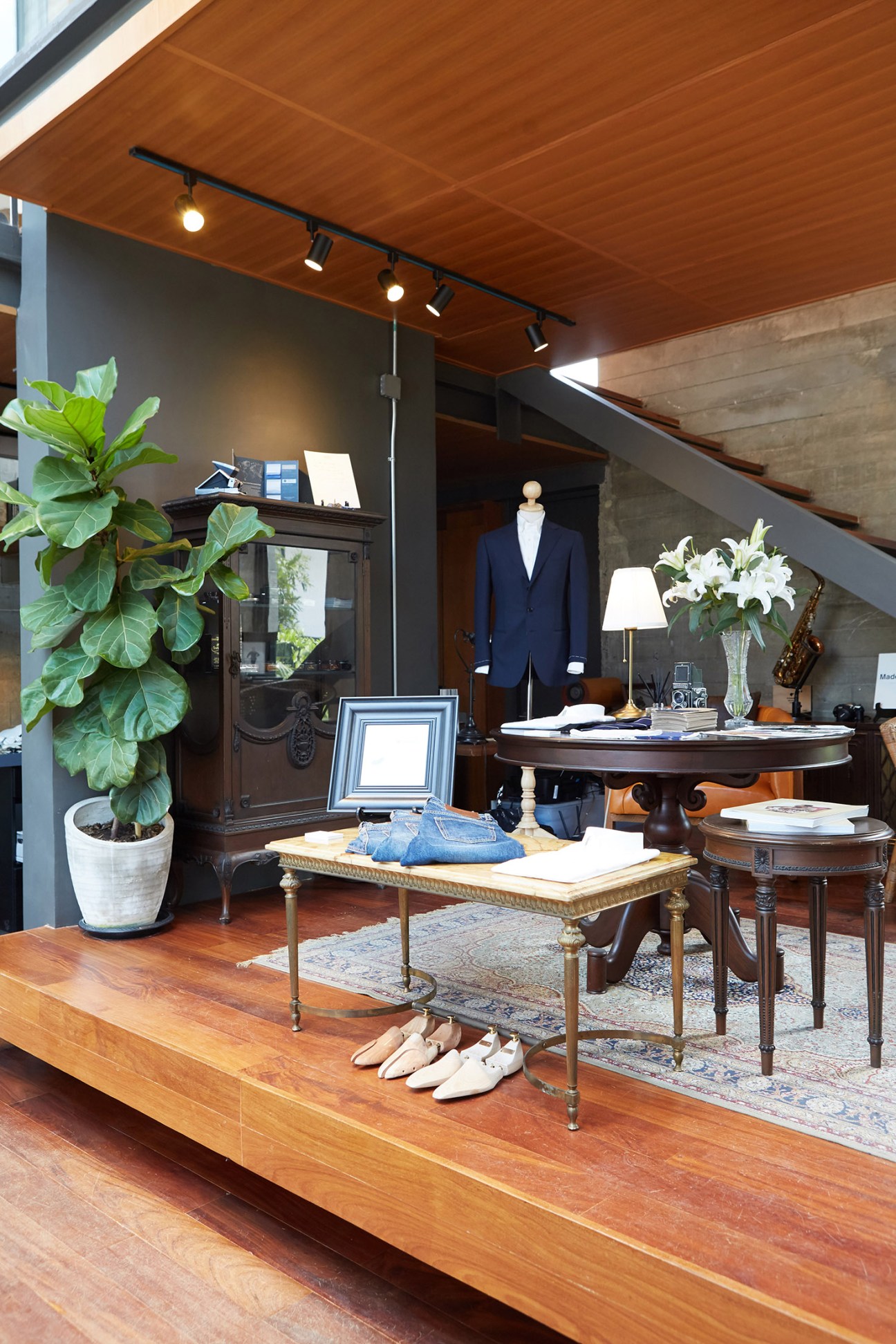 Studio Nicholson menswear display featuring a herringbone overcoat and marigold cashmere knit on a mannequin in a boutique setting.