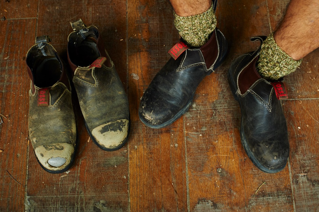 Two pairs of worn Rossi steel-toe boots displayed on a wooden floor with striped socks.