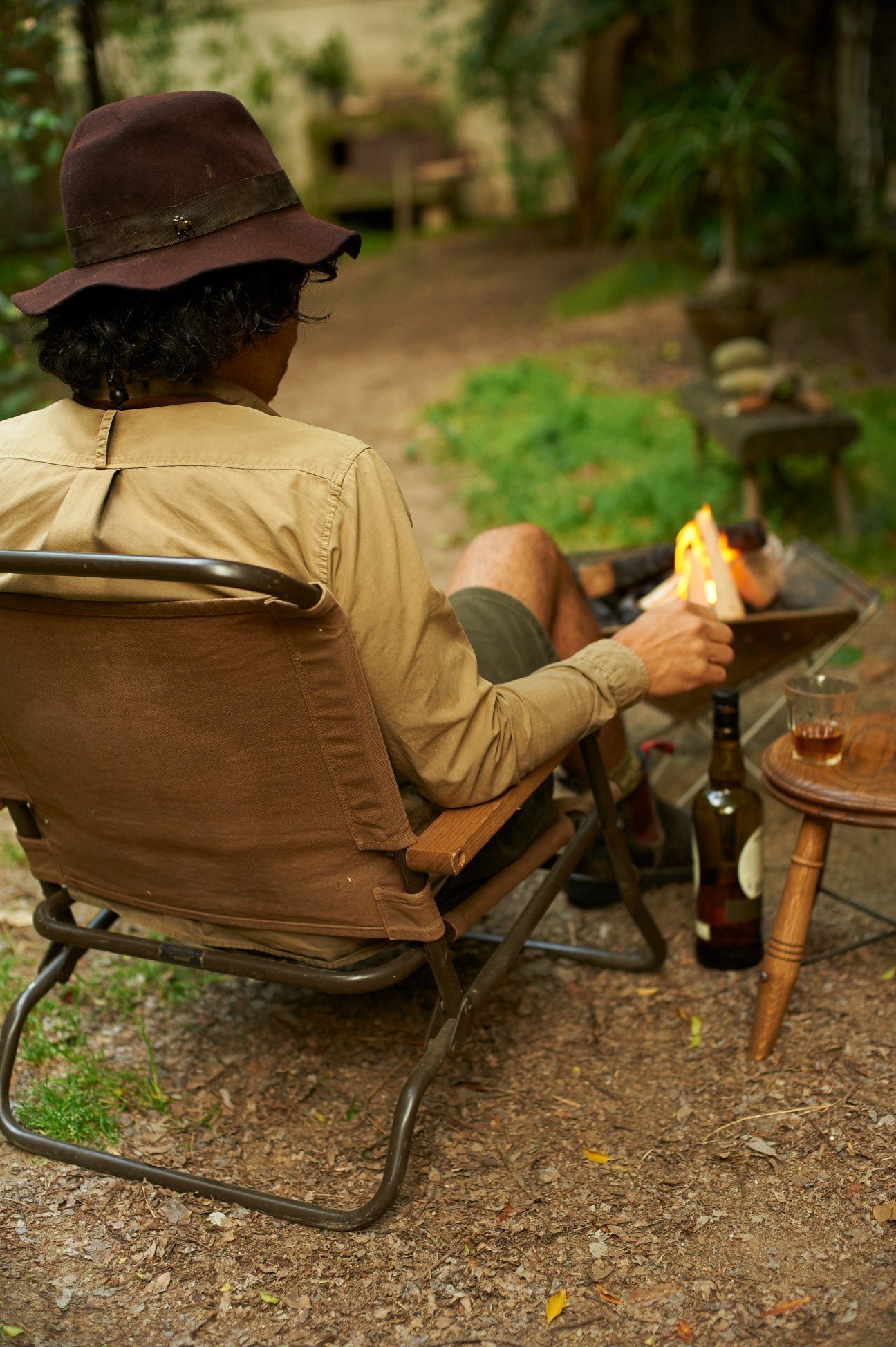 Person sitting in a low folding chair by a campfire in a garden setting.