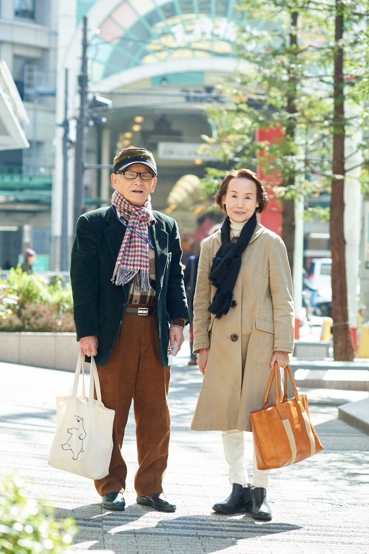 Elderly man and woman shopping together on a sunny street with modern architecture in background.
