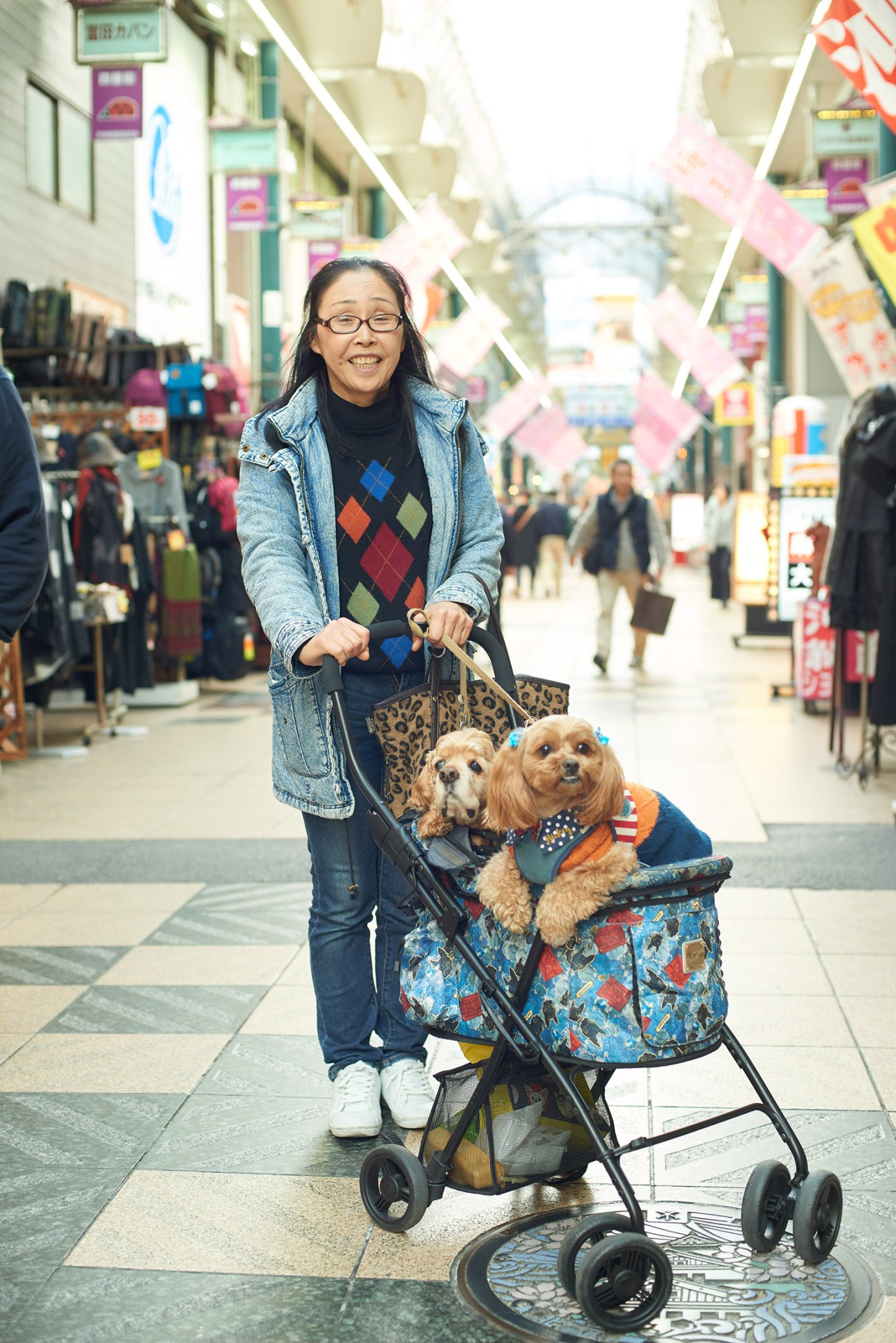 Woman pushing stroller with two dogs in a crowded shopping arcade in Osaka