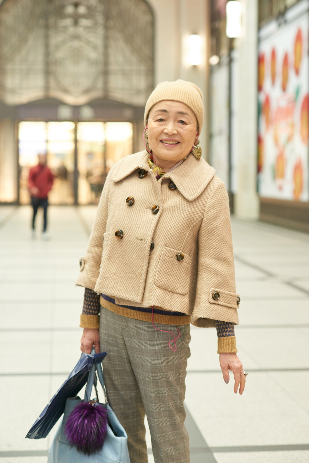 Woman wearing cream jacket and beige beanie carrying shopping bags on urban street