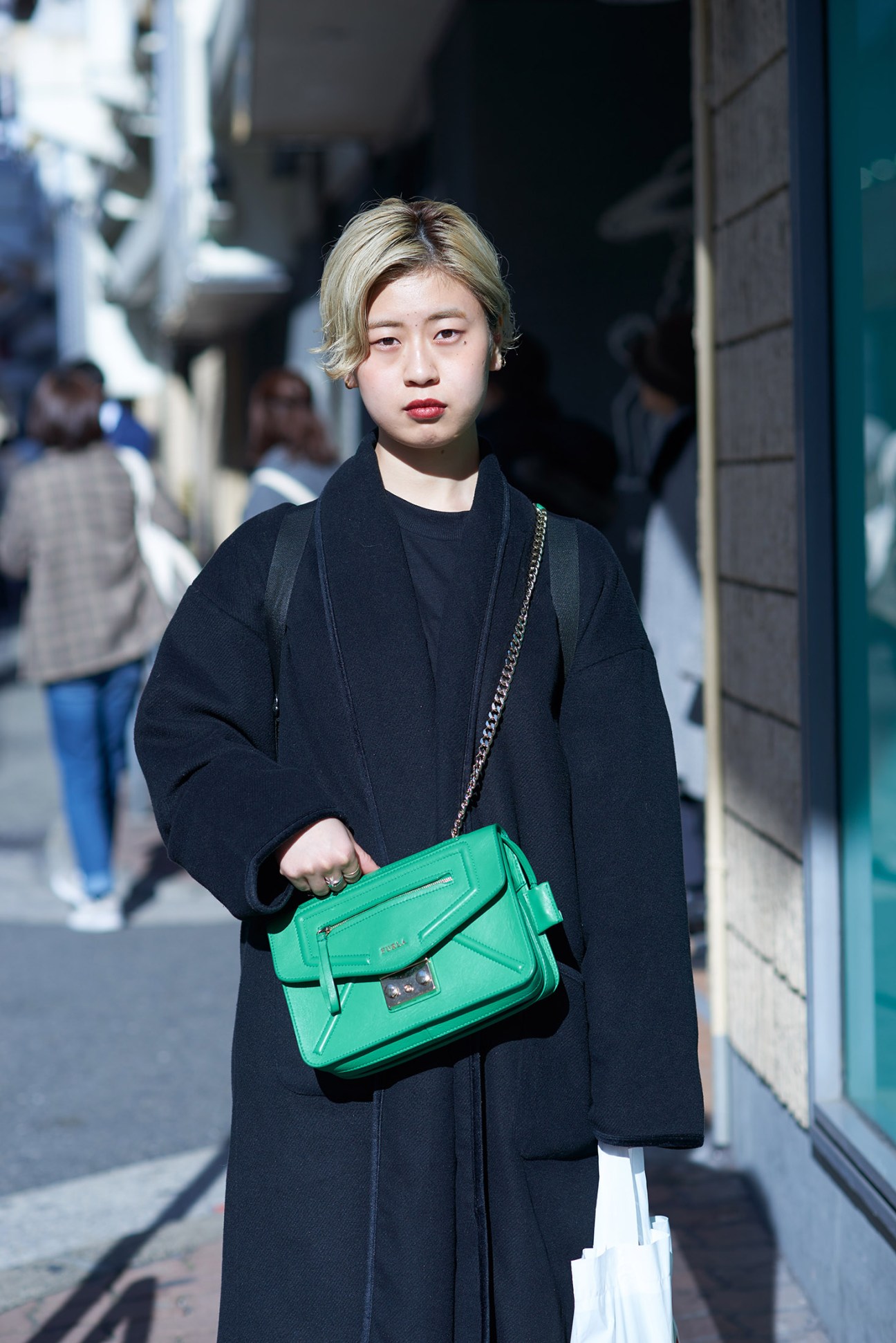 Young woman in black coat carrying a bright green shoulder bag on a city street.