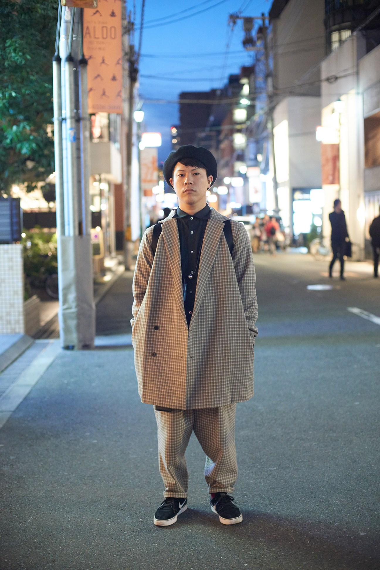 Young man in tan checkered suit and black shirt standing on Osaka street at dusk.