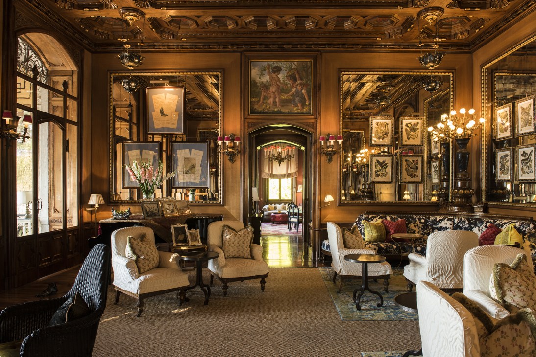 Ornate hotel lobby with gold paneling, framed artwork, elegant furniture, and chandelier lighting at Villa Feltrinelli.