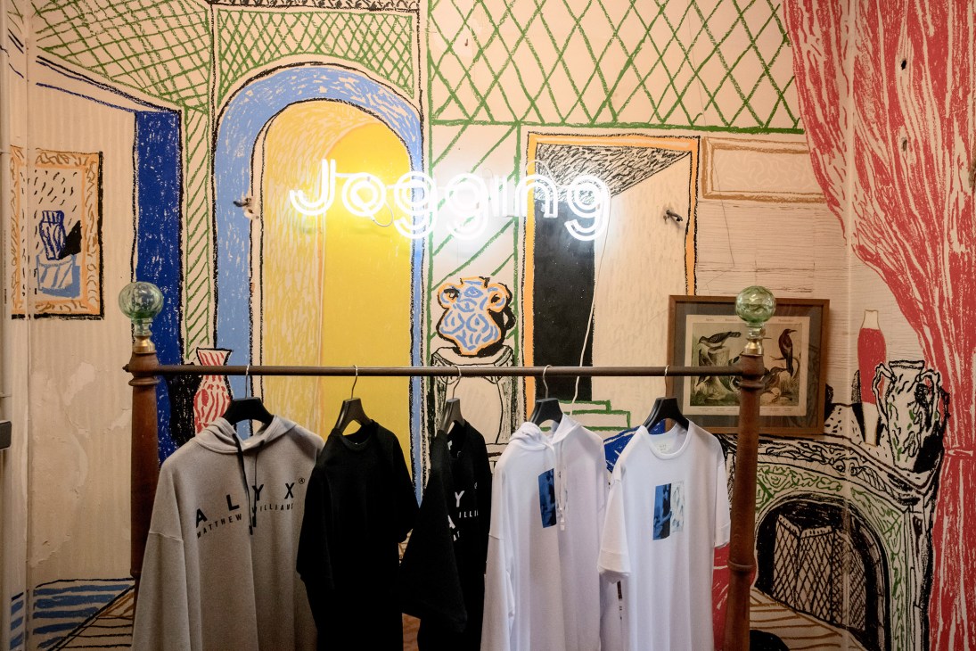Jogging boutique storefront with neon sign, displaying clothing on hangers against colorful patterned wall art.