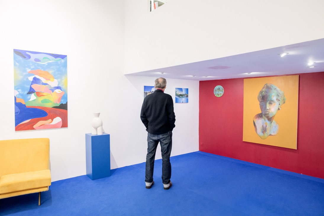 Man viewing contemporary artworks in a bright gallery space with colorful walls and abstract paintings.